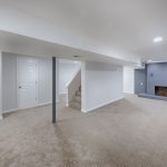 a finished basement with grey fireplace and tan carpeting